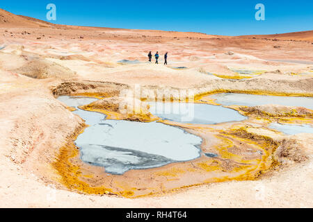 Trois touristes marcher par la boue des fosses, des fumerolles et des geysers de Sol de Manana près de la télévision sel Uyuni (Salar de Uyuni) dans l'Altiplano de Bolivie. Banque D'Images