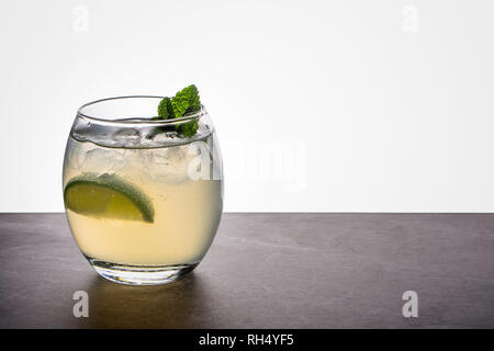 Un mojito cocktail dans un petit verre ovale garni de Menthe et citron vert sur un rocher de pierre et de base arrière-plan éclairé Banque D'Images