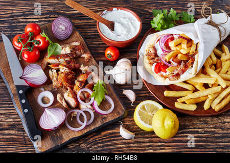 Vue aérienne de grec pita souvlaki, gyros avec ma viande de poulet, légumes, frites et sauce à l'ail, le yaourt Ingrédients sur une planche à découper sur Banque D'Images