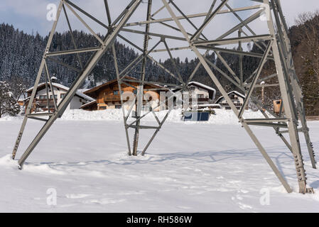 Maisons à énergie solaire photovoltaïque panneaux photovoltaïques vu à travers un pôle de puissance haute tension. Un jour d'hiver ensoleillé et tout couvert de neige. Banque D'Images