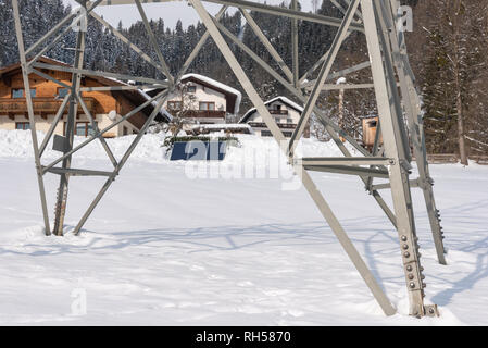 Maisons à énergie solaire photovoltaïque panneaux photovoltaïques vu à travers un pôle de puissance haute tension. Un jour d'hiver ensoleillé et tout couvert de neige. Banque D'Images