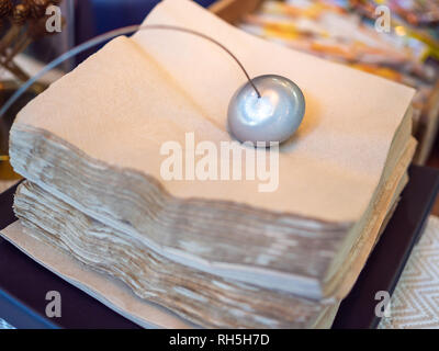 Close-up design métal paperweight sur pile de serviettes de table marron sur la table à café. Banque D'Images