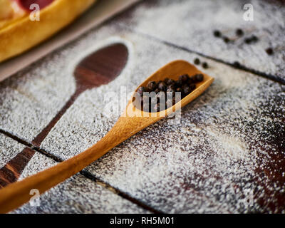 Poivre noir dans une cuillère en bois sur la table de cuisine Banque D'Images