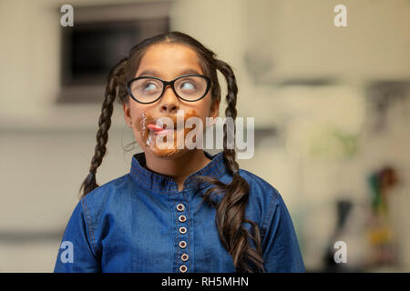 Girl wearing eyeglasses léchant le chocolat autour de sa bouche jusqu'à la Banque D'Images