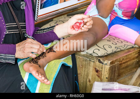 Durban, Afrique du Sud - Janvier 6th, 2019 : une femme musulmane en peinture au henné sur la cheville d'une jeune fille au centre de la ville de Durban, Afrique du Sud. Banque D'Images