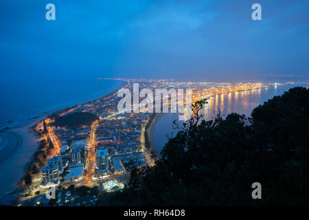 Les lumières de nuit urbaine haut de monument Mount Maunganui une touriist ville destination populaire ci-dessous avec plage sur l'océan d'un côté et le port . Banque D'Images