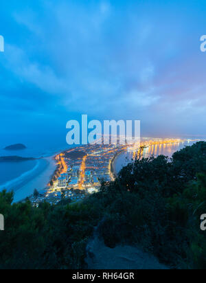 Les lumières de nuit urbaine haut de monument Mount Maunganui une touriist ville destination populaire ci-dessous avec plage sur l'océan d'un côté et le port . Banque D'Images