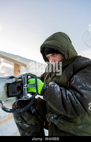 Travaux d'installation avec une tronçonneuse dans les mains de bloc de glace inférieurs Banque D'Images