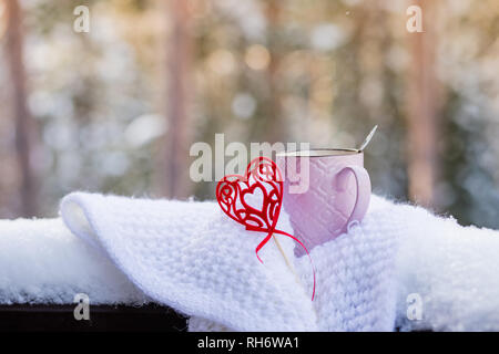 Tasse avec coeur rouge et une boisson chaude enveloppée dans un foulard dans la neige. Concept pour la Saint-Valentin romantique.Le petit déjeuner du matin pour la Saint-Valentin on snowy Banque D'Images