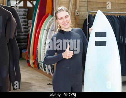 Heureux femme surf club formateur en combinaison, comité permanent outdoor with surfboard Banque D'Images