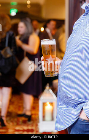Man with beer belly tenant une pinte de bière dans sa main lors d'un événement. Les gens à l'arrière-plan. Banque D'Images