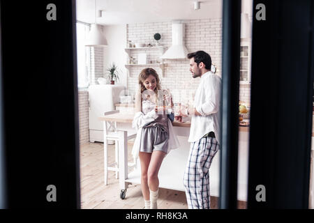 Jolie jeune femme aux cheveux longs et son mari prenant le petit déjeuner avec eux Banque D'Images