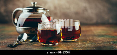 Théière en verre transparent et deux tasses en verre avec le thé noir sur un tableau sombre Banque D'Images