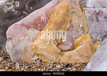 Rock couleur rouge jaune gris avec lignes striées l'un des nombreux rochers sur Goring beach Worthing UK. Celui-ci a des couleurs vibrantes sur un lit de galets. Banque D'Images