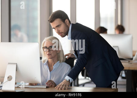 Homme sérieux supervision mentor employée s'aider avec un problème informatique Banque D'Images