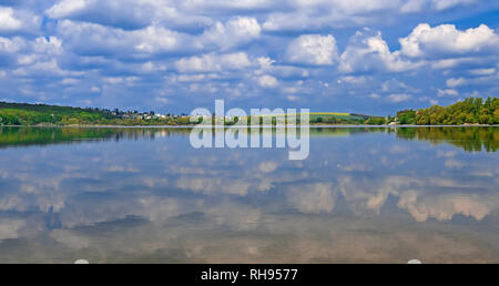 Un pont mène à une île au milieu d'un lac sur lequel de grands arbres verts croître contre un ciel bleu avec des nuages Banque D'Images