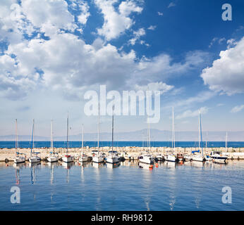 Voile et bateaux de pêche dans un port sous un ciel nuageux. Banque D'Images