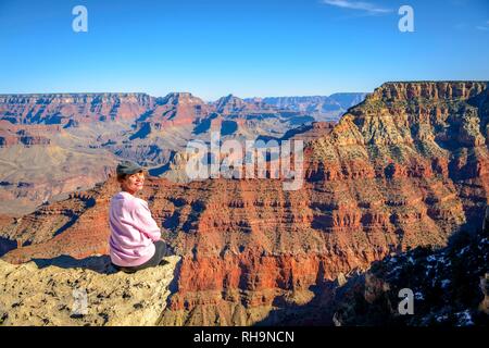 Jeune femme souriante, assise à l'abîme de la gorge gigantesque du Grand Canyon, vue depuis le sentier littoral, entre Mather Banque D'Images