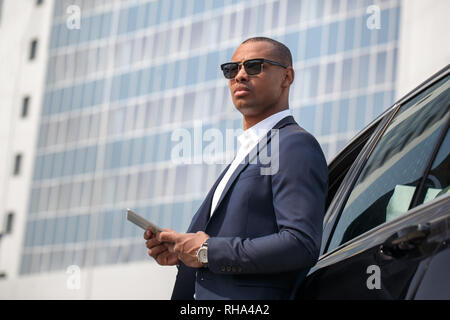 Jeune homme portant des lunettes de mulâtre debout appuyée sur location holding digital tablet à côté des Banque D'Images