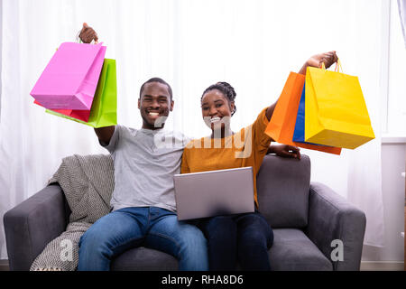 Portrait Of A Young Couple With Laptop Holding Colorful Shopping Bags Banque D'Images