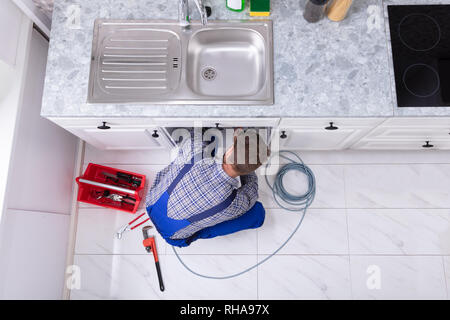 Jeune homme Nettoyage Plombier lavabo bouché dans la cuisine du tuyau Banque D'Images