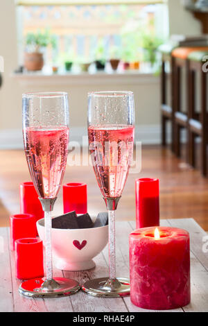 Deux verres de vin mousseux rose sur une table dans l'idée d'espace ouvert salon/salle à manger. Bougies rouge et chocolat suggérez un special Banque D'Images