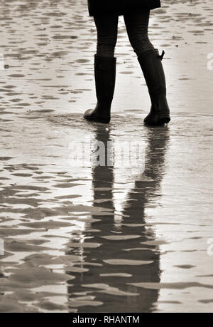 Figure féminine portant prêt bottes humides marche sur une plage de sable à marée basse Banque D'Images