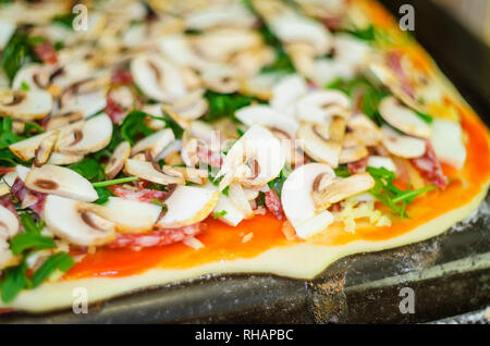 Processus de fabrication de pizzas. Italian Pizza au pepperoni, avec champignons, tomates, mozzarella, roquette, l'ail et la sauce Banque D'Images