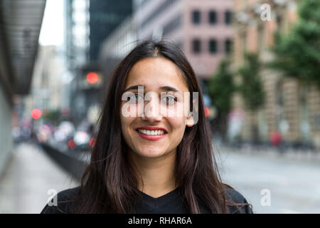 Belle jeune femme à la peau d'olive avec les yeux de couleur claire à l'extérieur permanent en milieu urbain et de sourire. Banque D'Images