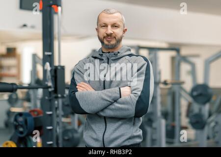 Portrait de l'homme sportif avec les mains jointes dans une salle de sport, beau formateur barbu regardant la caméra. Banque D'Images