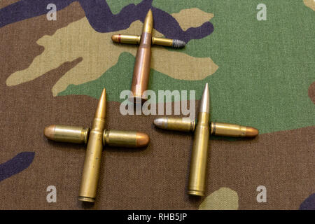 Des balles de fusil et de pistolet réunis dans la forme d'une croix. Concept de guerre. Fond tissu militaire shot. Banque D'Images