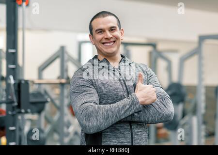 Portrait of smiling man sportive musculaire showing Thumbs up in gym, beau trainer regardant la caméra. Banque D'Images