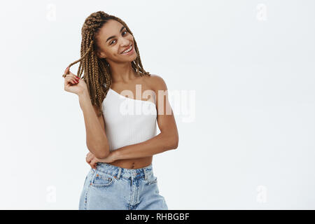 Elle sait comment le charme avec ces yeux. Portrait de charmant flirty african american woman with dreads jouant avec dreadlock et souriant sensully Banque D'Images