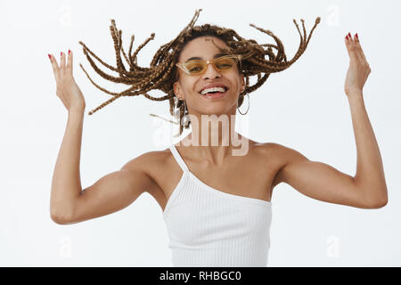 Cool Girl enjoying new hairstyle étant prêt à party rock. Portrait d'insouciance joyeuse femme à la peau sombre élégant avec des dreads dans des lunettes de soleil et haut Banque D'Images