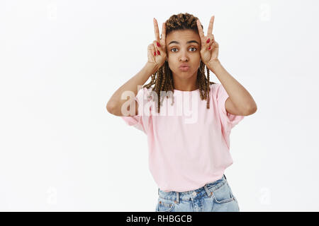 Girl making silly face tout en se posant contre le mur gris. Portrait de charmant et élégant féminin african american woman with dreads tacaud mignon Banque D'Images