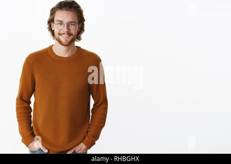 Plan de taille agréable attrayant barbu avec les cheveux longs et boucles dans les verres et pull-over chaud et amical sourire heureux en tenant l'appareil photo Banque D'Images