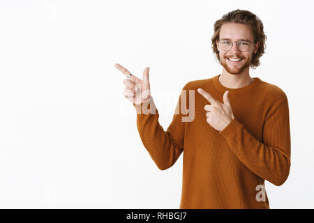 Jusqu'à la taille de balle-amical de charme à heureux jeune homme à barbe, dans les verres et souriant joyeusement comme pull pointant dans le coin en haut à gauche avec Banque D'Images