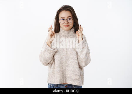 Portrait d'optimsitic heureux et excités par le jeune femme dans les verres et les doigts, à la croix pull bonne chance smiling espère anticiper miracle venu Banque D'Images