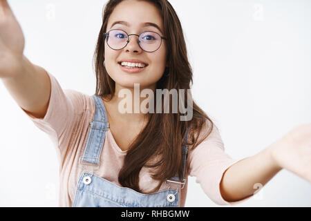 Fille d'atteindre les mains pour appareil photo pour donner l'accolade et amical sourire Mignon mignon raisng sourcils, le port de verres transparents et de salopettes en denim Banque D'Images