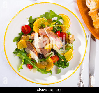 Vue de dessus de la salade de filets de canard coloré avec roquette fraîche, tomates, oignons frits, des tranches de fromage, de pruneaux et d'orange servi sur plaque blanche Banque D'Images