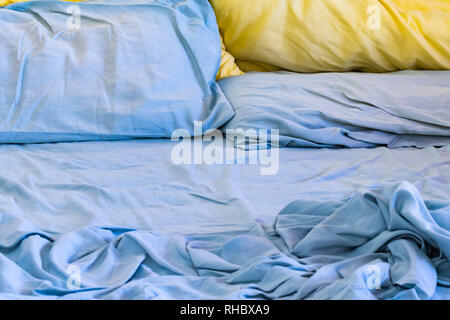 Lit défait malpropre avec feuilles bleu et oreillers bleu et jaune Banque D'Images