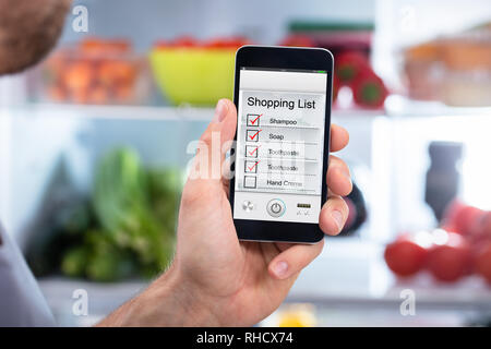 Close-up de la main de l'homme Contrôle de la liste d'achats sur Mobilephone en face de réfrigérateur Banque D'Images