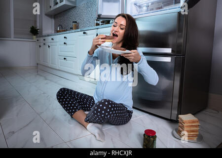 Young pregnant woman Eating Donut carrelage dans la cuisine Banque D'Images