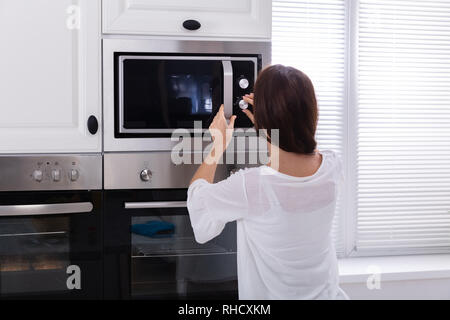 Vue latérale d'une jeune femme à l'aide d'un four micro-ondes four dans la cuisine Banque D'Images