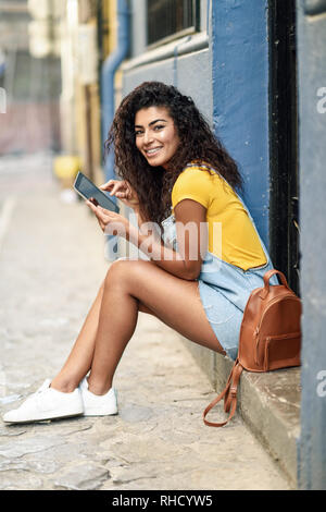 Heureux femme arabe assise sur l'étape urbaine avec une tablette numérique Banque D'Images