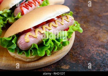 De délicieux hot-dogs avec saucisses grill, ketchup, moutarde, laitue, tomates sur un plateau en bois Close up Banque D'Images