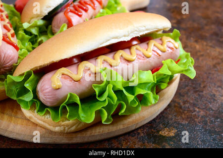 De délicieux hot-dogs avec saucisses grill, ketchup, moutarde, laitue, tomates sur un plateau en bois Close up Banque D'Images