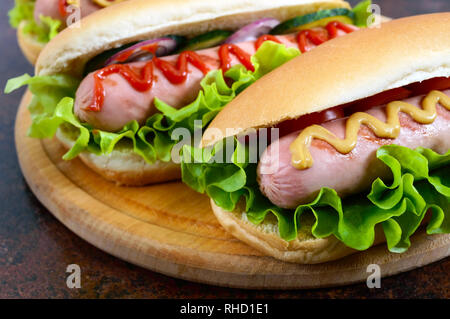 De délicieux hot-dogs avec saucisses grill, ketchup, moutarde, laitue, tomates sur un plateau en bois Close up Banque D'Images