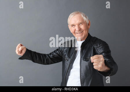 Hauts homme portant veste en cuir noire isolés sur mur gris holding fists à succès sourire caméra Banque D'Images