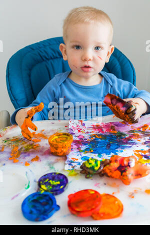 Garçon enfant dessine avec les peintures au doigt sur le papier à la table enfant Banque D'Images